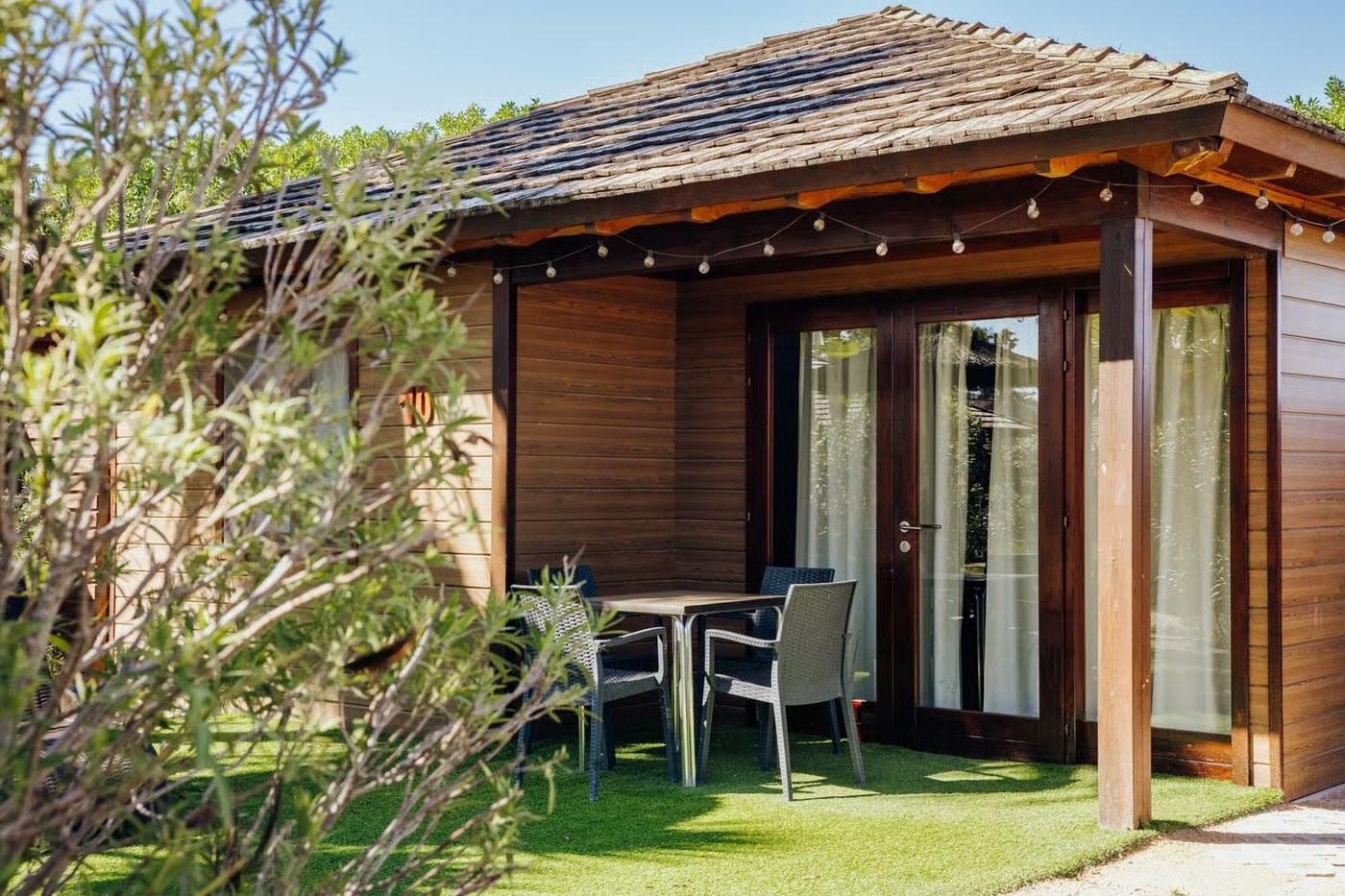 Bungaló de madera con porche, mesa y sillas sobre el césped en un camping de la Costa Blanca